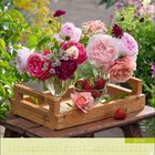 Juni, Kalenderblatt. Vase mit bunten Rosen und Erdbeeren auf einem Holztablett im Garten.