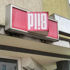 Der Text auf dem Schild lautet "BILD", ist jedoch auf dem Kopf stehend angebracht und befindet sich an einem Gebäude.