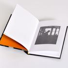 Kein Text erkennbar. Offenes Buch mit schwarz-weißem Bild einer Silhouette vor einem Fenster.