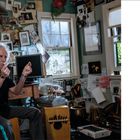 "IT'S ALL ABOUT TOUCH, IT'S NOT ABOUT POUNDING" steht groß auf der rechten Seite. Links sitzt ein Mann in einem mit Bildern vollgestellten Raum.