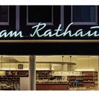 Neon-Schriftzug: "Fischer am Rathaus WEISSBROT". Darunter eine beleuchtete Bäckerei mit Schaufenstern.