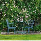 Text: „Happiness is not a destination“. Kleine Hütte mit grünem Dach im Garten, Holz stapelt sich darunter, Pflanzen ringsum.