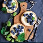 Kalender zeigt Juni. Drei Tartes mit Blaubeeren und Sahne auf Holzbrett, umgeben von Hopfenranken und Besteck.