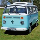 Nummernschild: "PAN WO 67H". Ein hellblauer VW-Bus steht auf einer grünen Wiese.