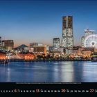 Text: „6 Juni 2023“. Skyline einer Stadt bei Nacht mit beleuchtetem Riesenrad und Wolkenkratzern am Wasser.