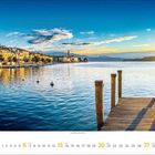 August 2023 Kalender. Abenddämmerung an einem See mit Booten und Schilfrohr, im Hintergrund Berge.