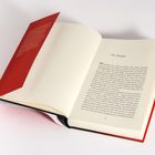 Text auf der linken Seite: unleserlich. Rechts: Kapitelüberschrift "1 Der Kampf" und Beginn eines Fließtextes. Buch hat roten Umschlag.
