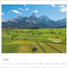 "Juni" steht unter einem Landschaftsbild: grüne Felder mit einem Golfplatz, dahinter beeindruckende Bergkette.