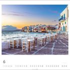 Tische und Stühle an einer Küste bei Sonnenuntergang. Kalender im Juni. Links das Meer, rechts weiße Gebäude.