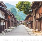 Kalender: Monat Juni mit Datumsangaben. Traditionelle Holzhäuser säumen eine leere Straße vor grünen Bergen.