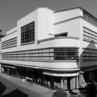 Die Schrift an Schildern lautet „moses“ und „dm“. Es ist ein modernes Gebäude im Bauhausstil mit großen Glasfenstern.