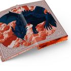 Ein großes, offenes Buch zeigt eine Illustration eines schwarzen Drachens mit roten Augen, der auf orangeroten Wolken schwebt.