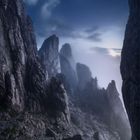 Felsige Berglandschaft mit hoch aufragenden Klippen im Nebel, umgeben von dunklem, wolkigem Himmel.