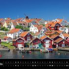 Schweden 06. Kalender mit Blick auf bunte Holzhäuser an einem Wasserufer unter blauem Himmel.