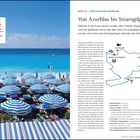 Eine Küstenlandschaft mit blauem Himmel und Meer. Blau-weiße Sonnenschirme stehen auf Reihen von Liegestühlen am Strand.