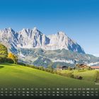 "Wilder Kaiser" vor imposanter Bergkette, grüne Wiesen im Vordergrund, einige Bäume und Hütten im Herbst. Kalenderdaten unten.