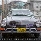Karmann Ghia 6. Gelbes Nummernschild „MAINE 442-208 VACATIONLAND“. Schwarzes Auto von vorne. Kopfsteinpflasterstraße.