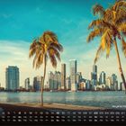"Skyline Miami Beach" und Kalenderdarstellung. Palmen im Vordergrund, dahinter Hochhäuser am Wasser bei blauem Himmel.