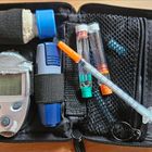 Ein offenes Etui mit Blutzuckermessgerät, Teststreifen, Lanzette, Insulinampullen und Spritze, alles sicher verstaut.