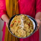 Ein Teller mit gewürztem Reis und Gemüse, gehalten von einer Person in einem pinken Gewand mit senfgelbem Schal.