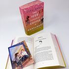 Das Buch "The Iced Caramel Coffee Agreement" von Kyra Groh steht neben einem offenen Buch. Eine Illustration zeigt zwei Personen auf einer Bank.