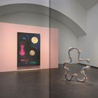 Große Gemälde mit geometrischen Formen auf rosa und weißem Hintergrund. Eine wellenförmige Skulptur in der Mitte.