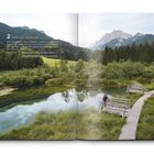 2. Bilderbuch-Landschaft. Smaragdgrünes Wasser, Wiesen, Wälder, graue Berge. Ein Steg mit Person in grüner Natur.