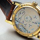 Goldene Uhr Rückseite, Text: A. LANGE & SÖHNE, Made in Germany, Nr. 2027. Sichtbare Uhrwerksmechanik mit braunem Lederband.