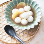 Eine Schale mit kleinen, weißen Kugeln in Flüssigkeit und zwei Ingwerscheiben. Darunter ein Bambuskorb und daneben ein Löffel.