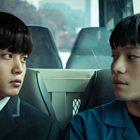 Zwei junge Männer in einem Bus, in formeller Kleidung, schauen sich intensiv an.