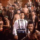 Große asiatische Schriftzeichen im Hintergrund. Eine Gruppe Männer, viele mit nacktem Oberkörper, teils mit Kopftüchern.