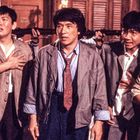 Eine Gruppe von Männern in Anzügen wirkt besorgt, im Hintergrund sind Gewehre zu sehen.