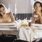 Zwei Frauen liegen auf Sonnenliegen. Eine Frau isst aus einer Schüssel, Getränke und Obst stehen zwischen ihnen.