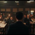 Mehrere Männer in Militäruniformen sitzen und stehen in einem Raum, der wie ein Besprechungsraum aussieht. Ein Mann steht im Vordergrund.
