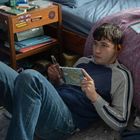 Ein Jugendlicher liegt auf dem Boden, hört mit Kopfhörern Musik und hält ein CD-Booklet.