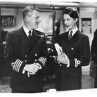 Zwei Personen in Marineuniformen stehen lächelnd miteinander in einem Büro. Links ein Mann, rechts eine Frau mit Dokumenten.