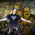 Auf dem T-Shirt steht: "Rise to Remain". Eine Person singt vor einem großen, gruseligen Hintergrundmotiv.
