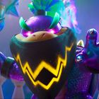 Eine bunte, mächtige Figur mit violetten Augen und einem leuchtenden Zickzackmuster auf einem schwarzen Halstuch.