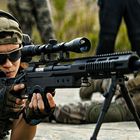 Ein Soldat zielt mit einem Scharfschützengewehr. Er trägt Kopfhörer, Sonnenbrille und eine umgedrehte Cappy.
