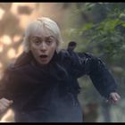 Eine Person mit blondem Haar rennt durch einen Wald, hinter ihr helle Explosionen oder Lichtblitze. Sie wirkt erschrocken.