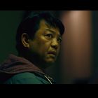 Ein Mann schaut nachdenklich zur Seite, seine Umgebung ist dunkel ausgeleuchtet.