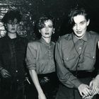 Fünf Personen in einem düsteren Raum, alle mit stylischen 80er-Jahre-Outfits und dramatischen Ausdrücken.