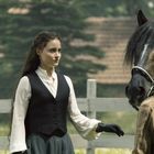 Zwei Frauen stehen mit einem schwarzen Pferd auf einer Weide. Eine Frau trägt Handschuhe. Im Hintergrund sind gefleckte Dächer.