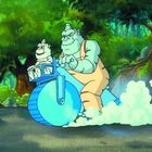 Zwei blaue, cartoonartige Kreaturen fahren ein ungewöhnliches Motorrad durch einen grünen Wald.