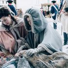 Zwei Frauen in historischen Wintermänteln hocken besorgt neben einem älteren Mann, der im Schnee liegt.