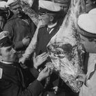 Mehrere Männer in Matrosenuniformen inspizieren interessiert Beine von einem großen Tierkopf.