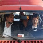 Eine Frau und ein Mann sitzen in einem roten Auto. Der Mann schaut die Frau an, während sie nach unten blickt.