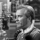 Ein Mann im Profil trägt historisches Kostüm mit Rüschenkragen. Im Hintergrund Kerzenständer.