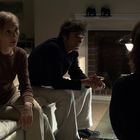 Zwei Personen sitzen auf einem Sofa, ein Mann und eine Frau, in einer gemütlichen, schummrig beleuchteten Umgebung.