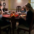 Vier Personen sitzen um einen Tisch mit einem Truthahn. Ein Hund liegt auf einer Decke im Hintergrund.